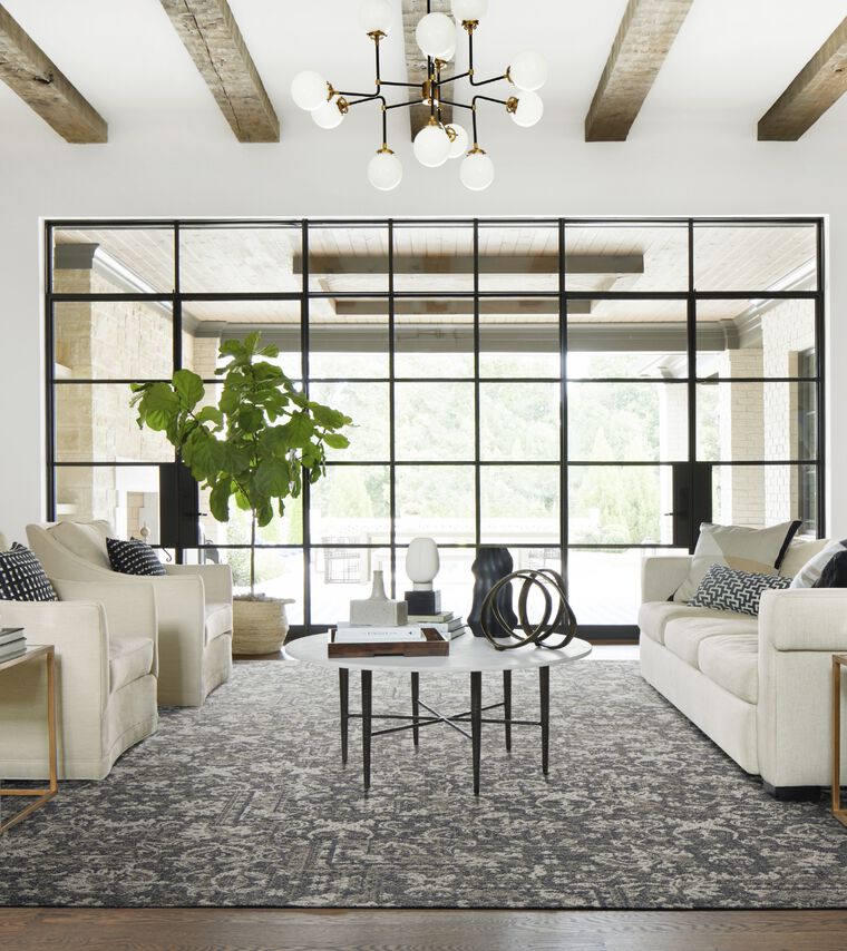 Grand living room with wood beams and wall of windows featuring FLOR Fancy Free area rug shown in Pigeon